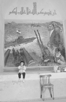 Young girl sitting under a mural of General Abd (Gamal) al-Nasser, former president of Egypt, in the entryway of the Fort Qaitbey museum.