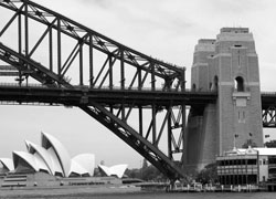 View from the ferryboat, showing the bridge (note ant-like climbers starting up on top), the pylons and, in the distance, the Sydney Opera House. Photo: Olander