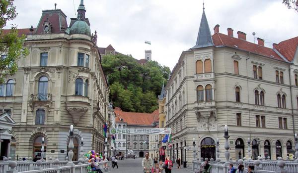 Walking the center span of Ljubljana’s decorative Tromostovje (Triple Bridge) toward hilltop Ljubljana Castle.